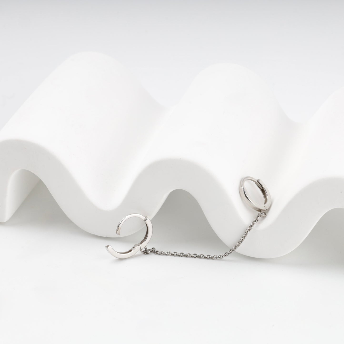 Polished silver huggie hoops joined by a chain, detail — Kabluchka