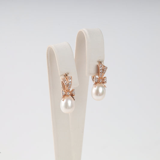 Elegant 14K (585) Rose Gold drop earrings featuring a sparkling zirconia-set bow and a lustrous teardrop pearl, secured with a classic English lock.