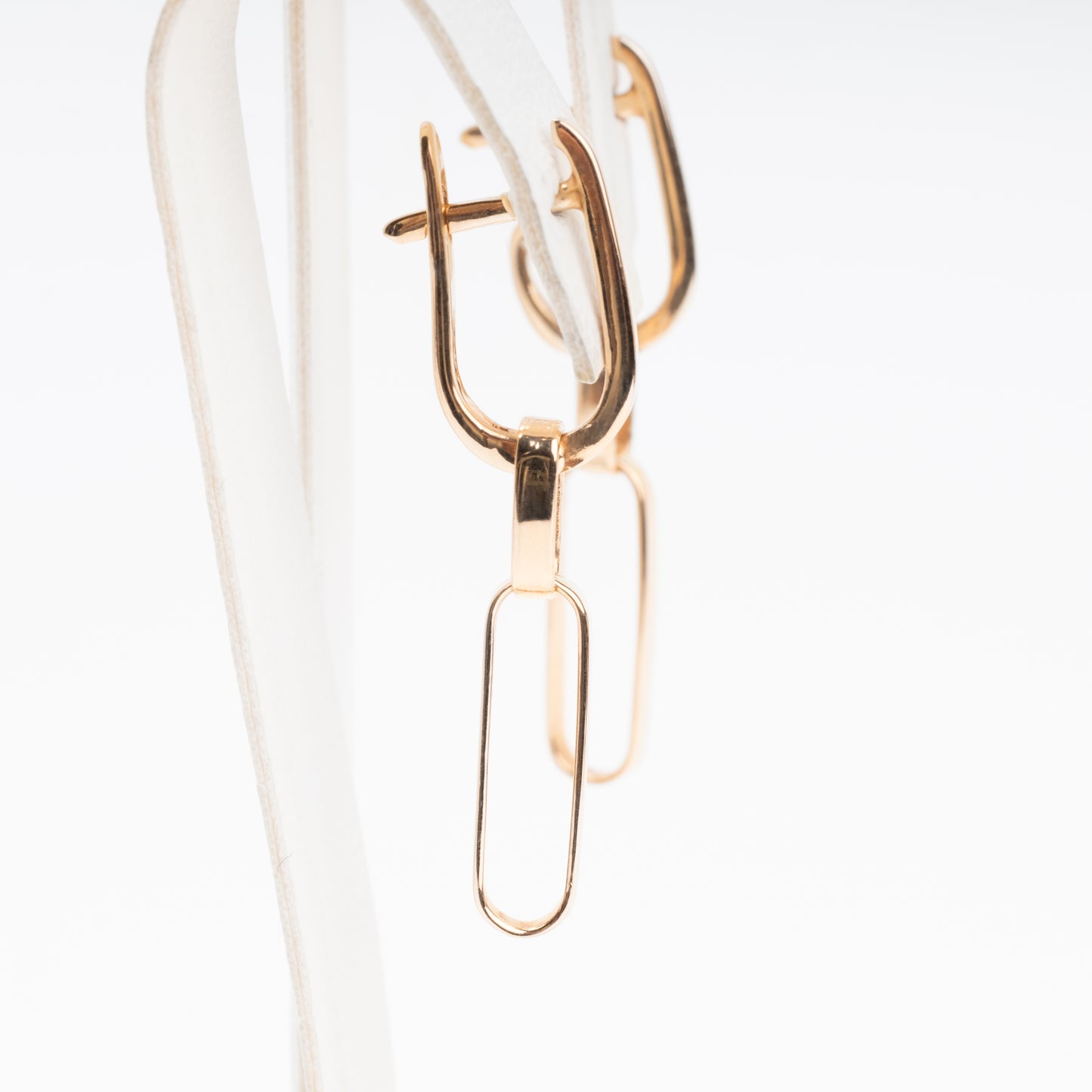 14k gold paperclip dangle earrings on a display stand, minimalist drop hoops, Ukrainian Jewelry for everyday wear.