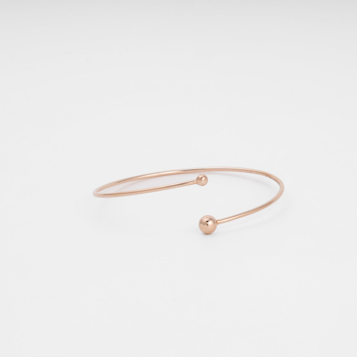 Minimalist 14k gold open bangle bracelet with two ball ends on white background, modern Ukrainian Jewelry for everyday stacking.