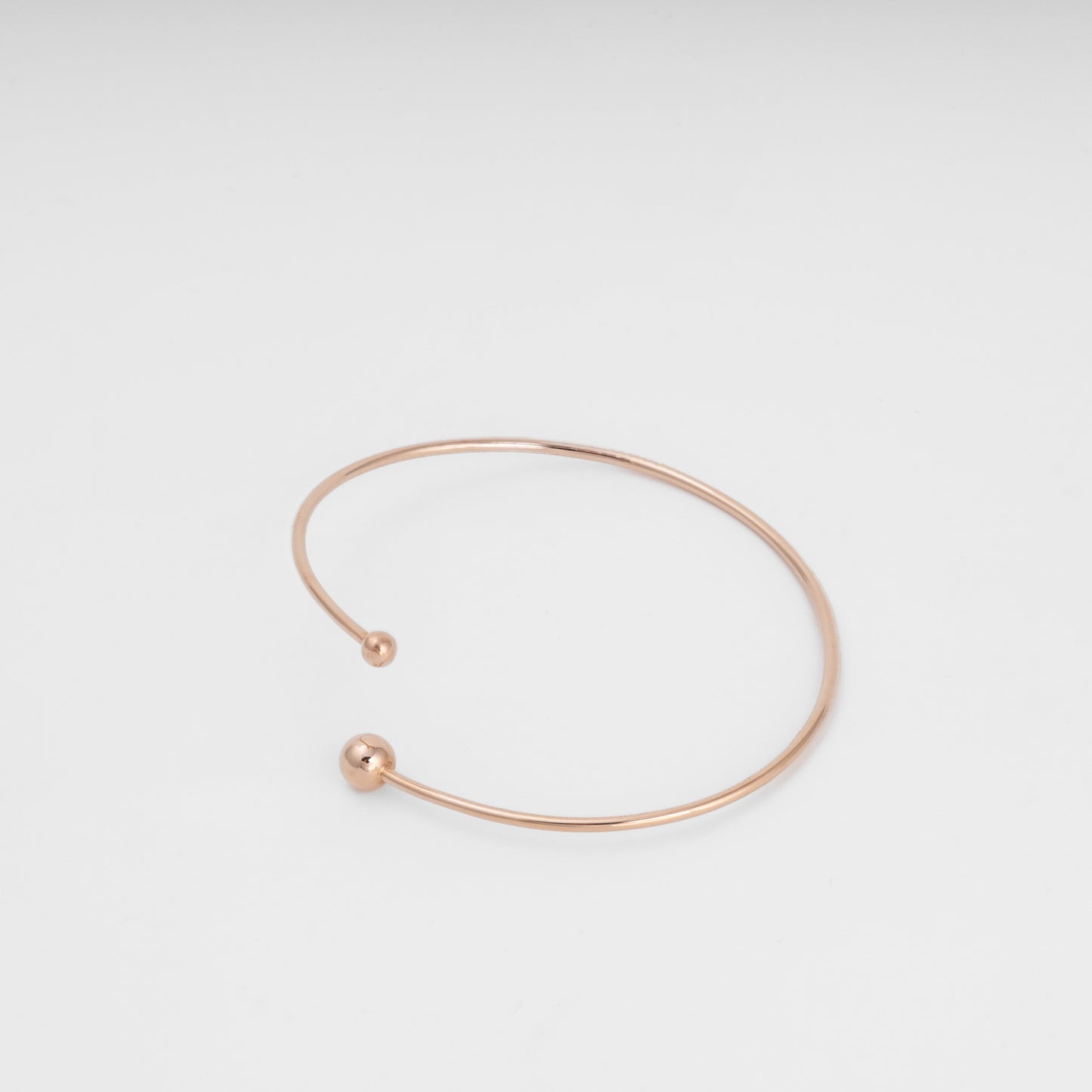 Minimal open 14k gold bangle bracelet with ball ends on white background, simple cuff Ukrainian Jewelry for everyday wear.