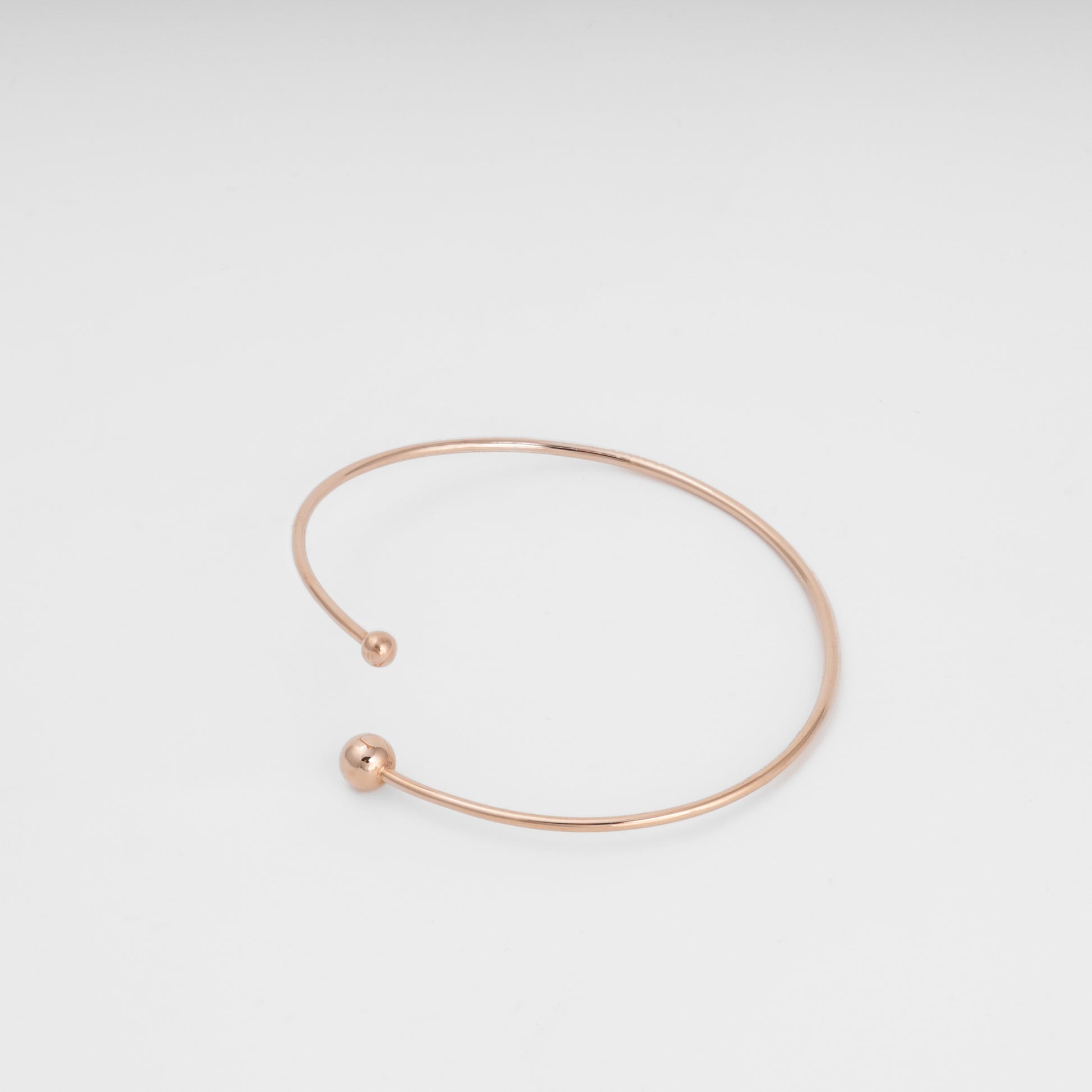 Minimal open 14k gold bangle bracelet with ball ends on white background, simple cuff Ukrainian Jewelry for everyday wear.