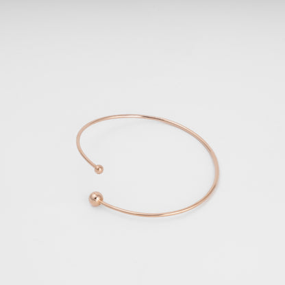 Minimal open 14k gold bangle bracelet with ball ends on white background, simple cuff Ukrainian Jewelry for everyday wear.