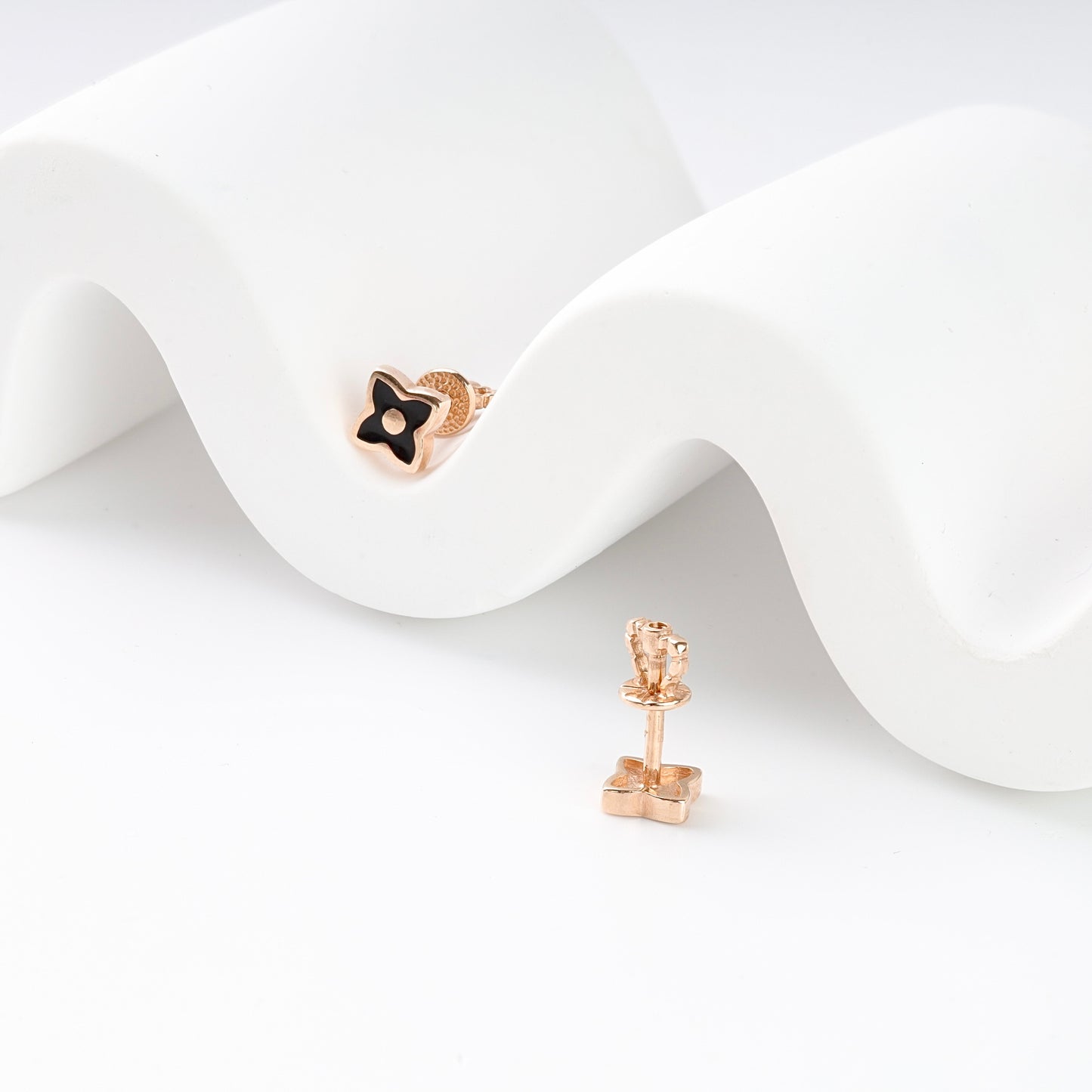 Elegant 14K (585) Rose Gold and black clover studs on a modern white textured background, showcasing their dainty and neat size.