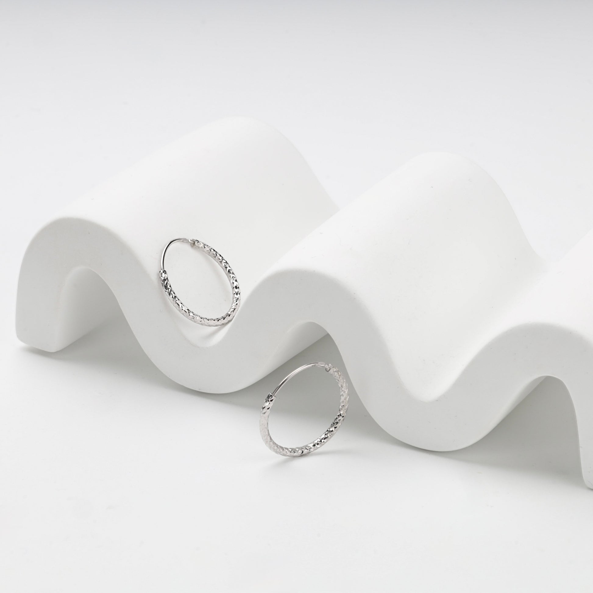 Slim silver hoop earrings with faceted diamond-cut texture