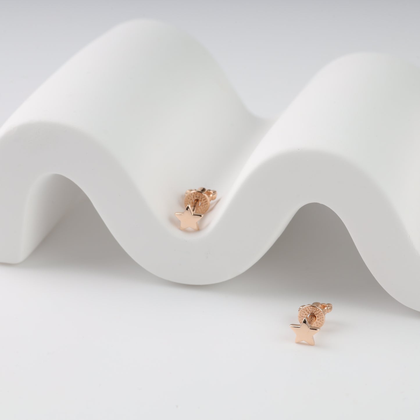 Rose gold earrings on a white wavy surface