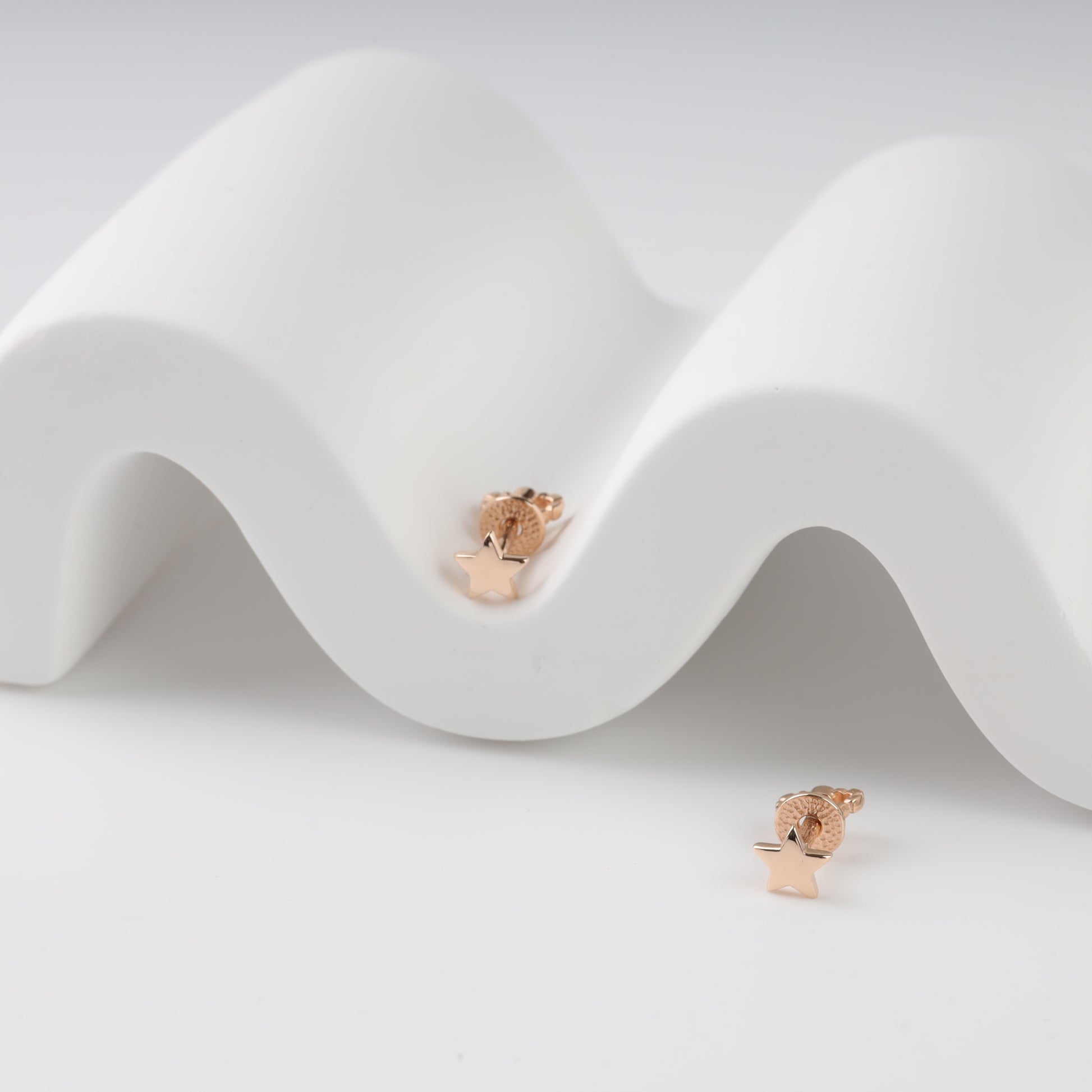 Rose gold earrings on a white wavy surface
