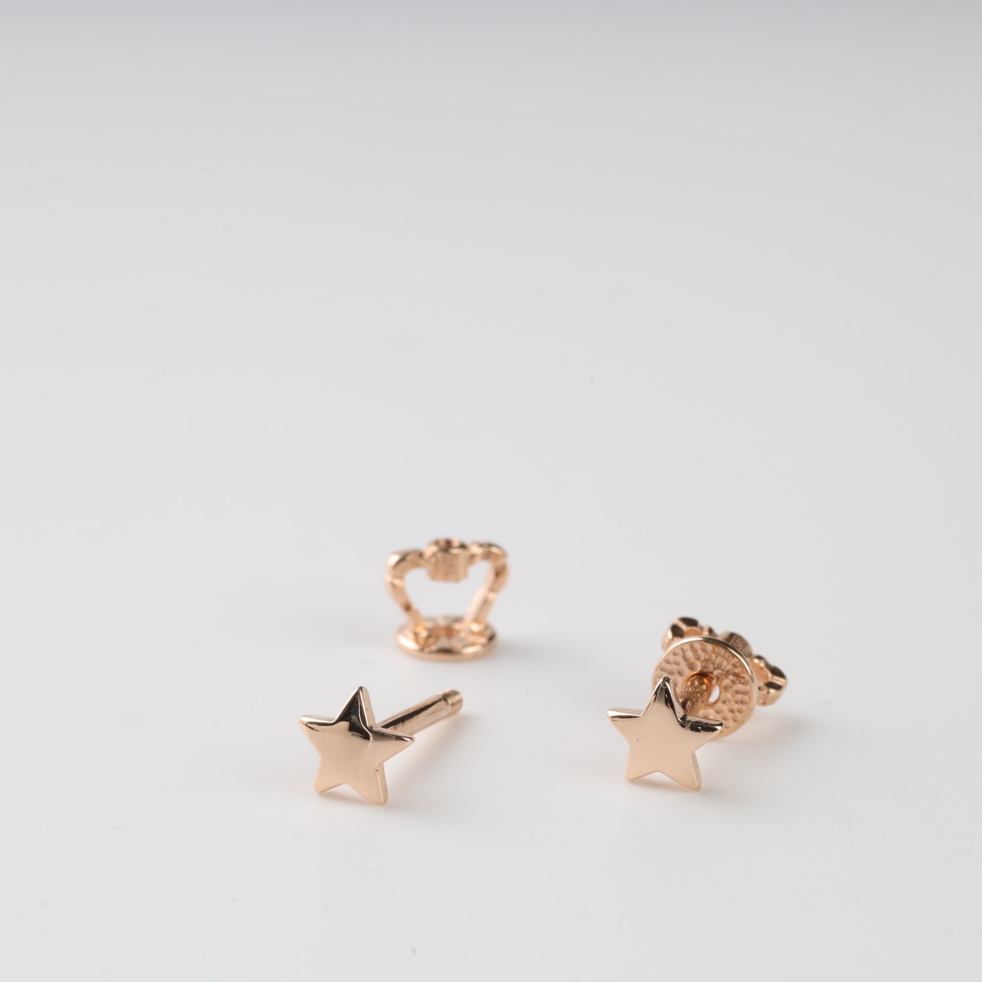 Rose gold star-shaped earrings on a light gray background