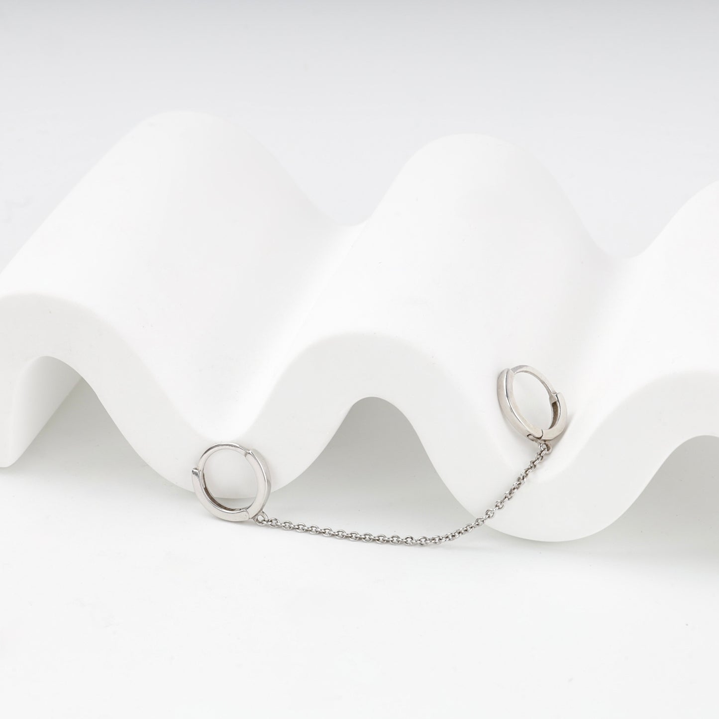Two small silver huggie hoops connected by a delicate chain — Kabluchka