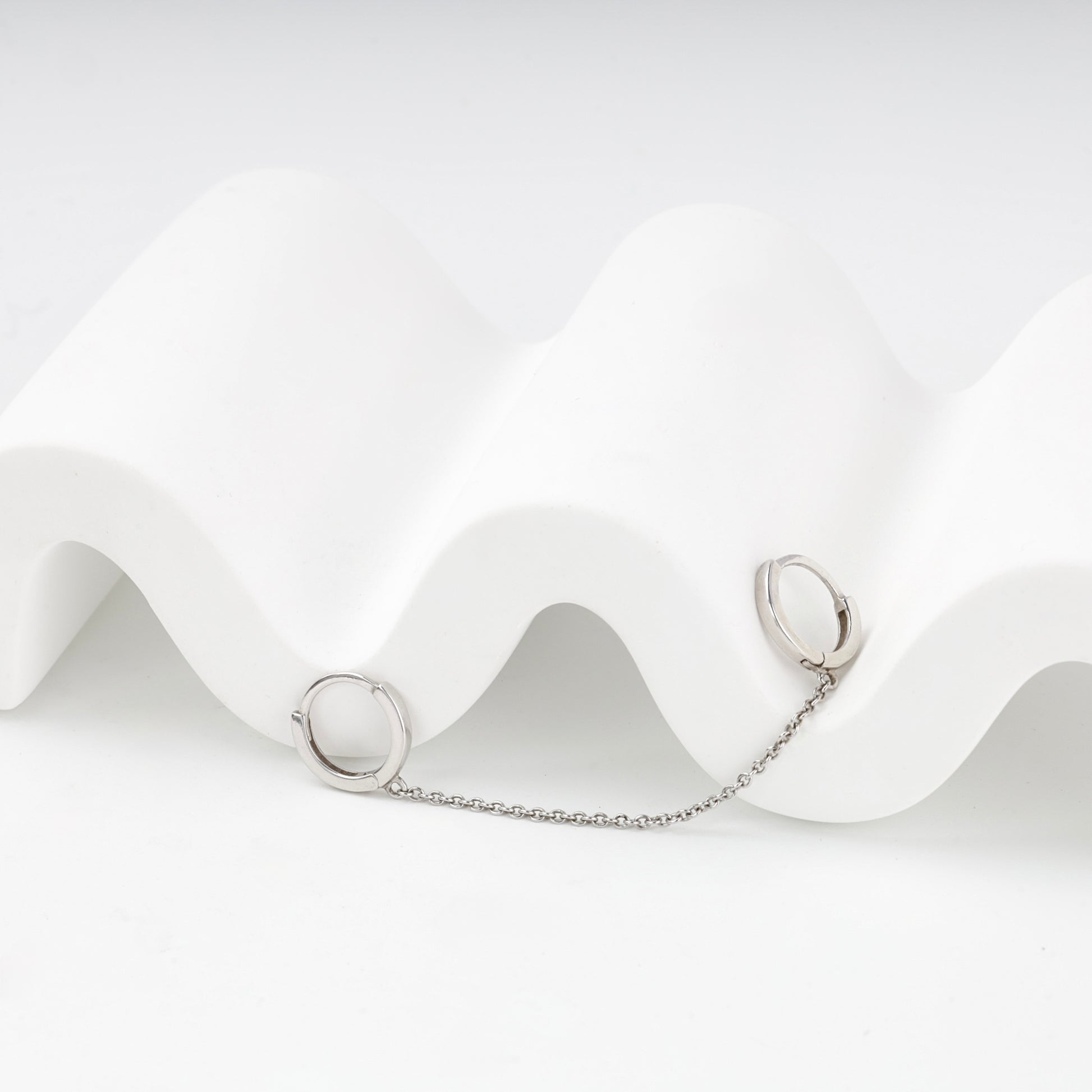 Two small silver huggie hoops connected by a delicate chain — Kabluchka