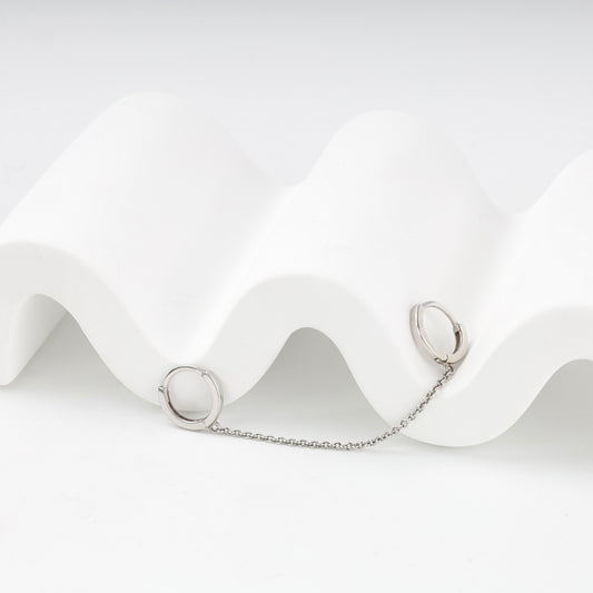Two small silver huggie hoops connected by a delicate chain — Kabluchka