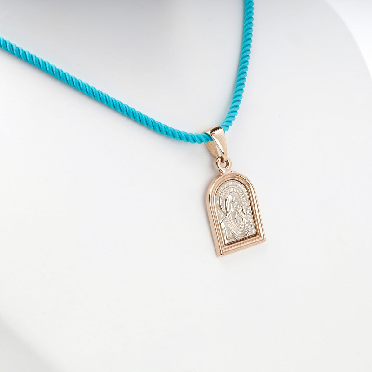 Two-tone gold religious pendant shown on a turquoise styling cord
