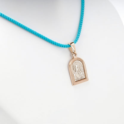 Two-tone gold religious pendant shown on a turquoise styling cord