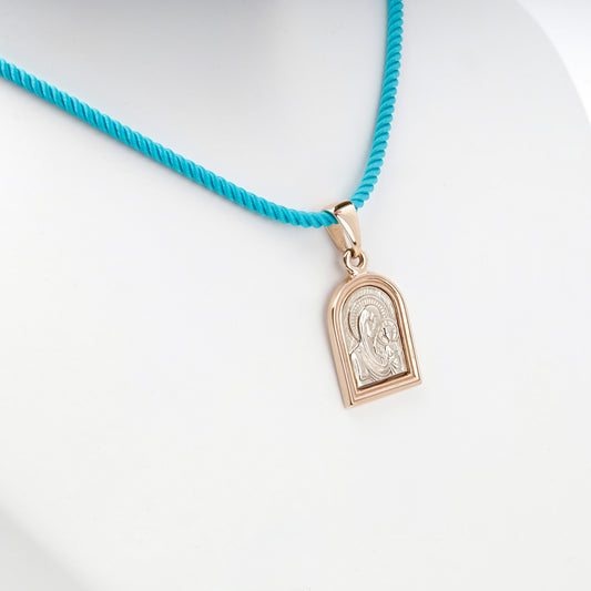Two-tone gold religious pendant shown on a turquoise styling cord