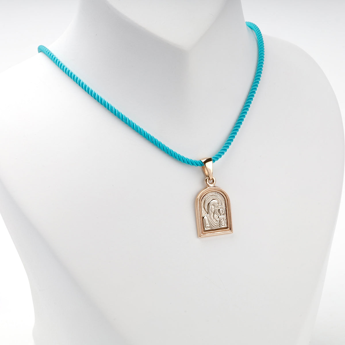 Two-tone gold icon pendant displayed on a turquoise styling cord