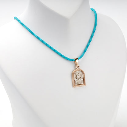 Two-tone gold icon pendant displayed on a turquoise styling cord