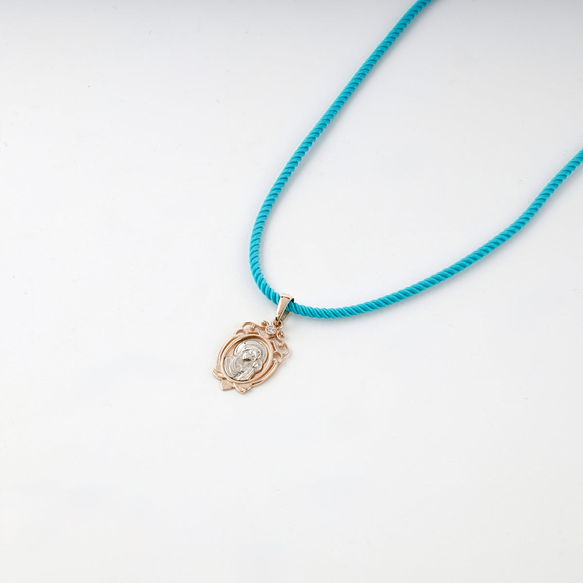 Two-tone gold icon pendant shown on a turquoise styling cord
