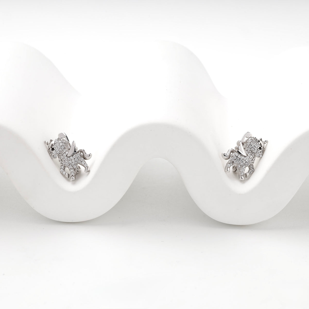 Silver unicorn earrings displayed on a white wave