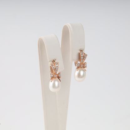 Elegant 14K (585) Rose Gold drop earrings featuring a sparkling zirconia-set bow and a lustrous teardrop pearl, secured with a classic English lock.