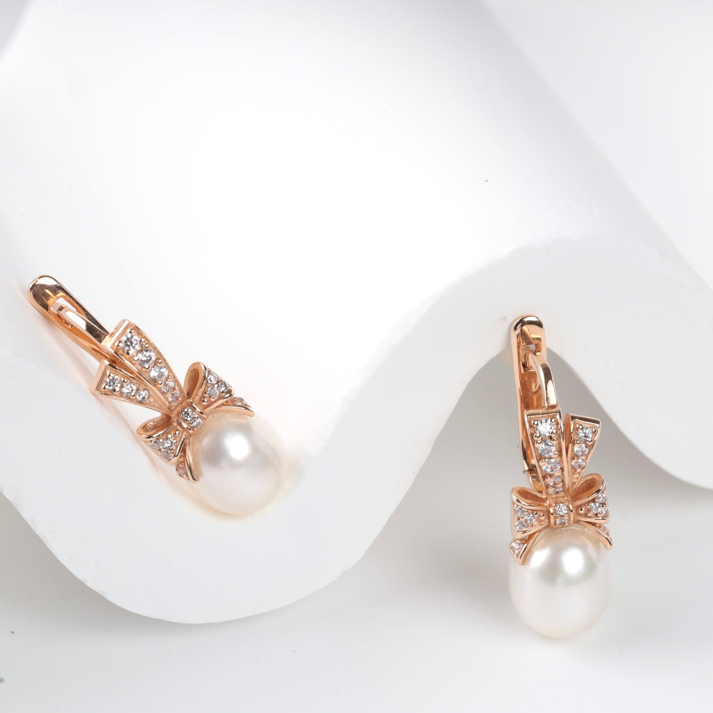 Elegant 14K (585) Rose Gold drop earrings featuring a sparkling zirconia-set bow and a lustrous teardrop pearl, secured with a classic English lock.