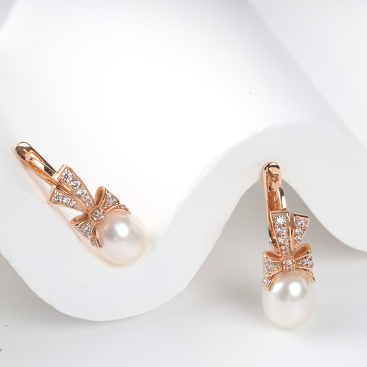 Elegant 14K (585) Rose Gold drop earrings featuring a sparkling zirconia-set bow and a lustrous teardrop pearl, secured with a classic English lock.