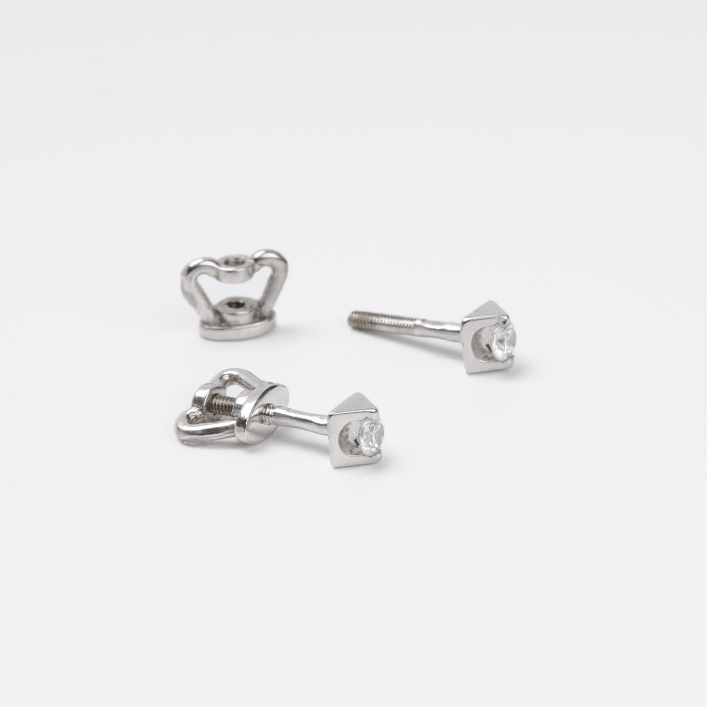 14K (585) White Gold geometric stud earrings and their corresponding screw-on locks displayed on a textured white surface, highlighting the brilliant metallic finish.