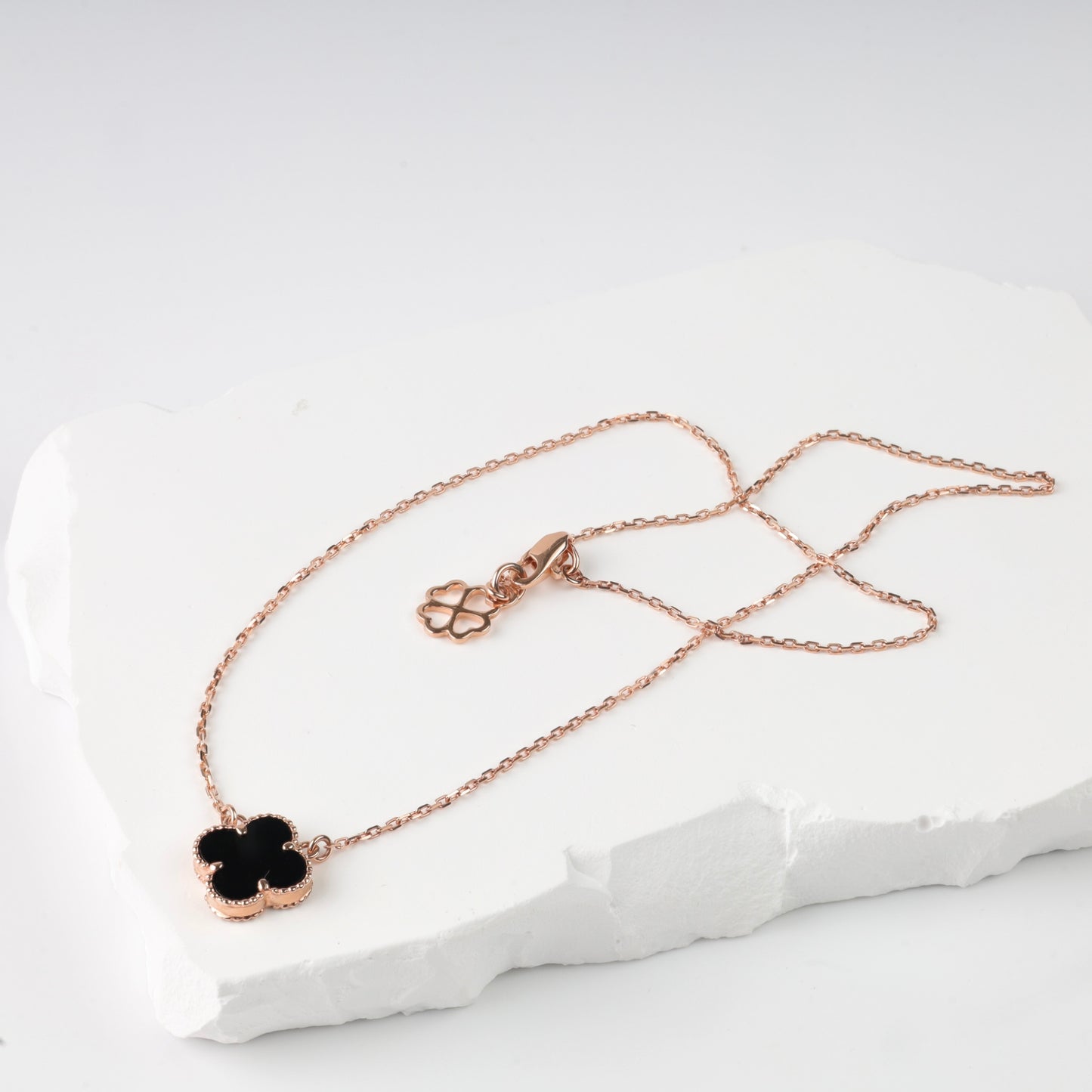 An elegant polished 14K (585) rose gold necklace featuring a delicate chain and a central four-leaf clover pendant. The insert is made of black onyx, framed by a detailed beaded rose gold border.