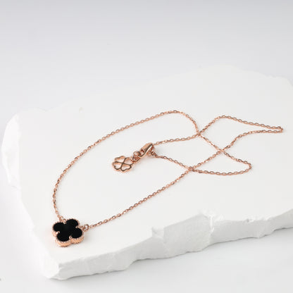 An elegant polished 14K (585) rose gold necklace featuring a delicate chain and a central four-leaf clover pendant. The insert is made of black onyx, framed by a detailed beaded rose gold border.