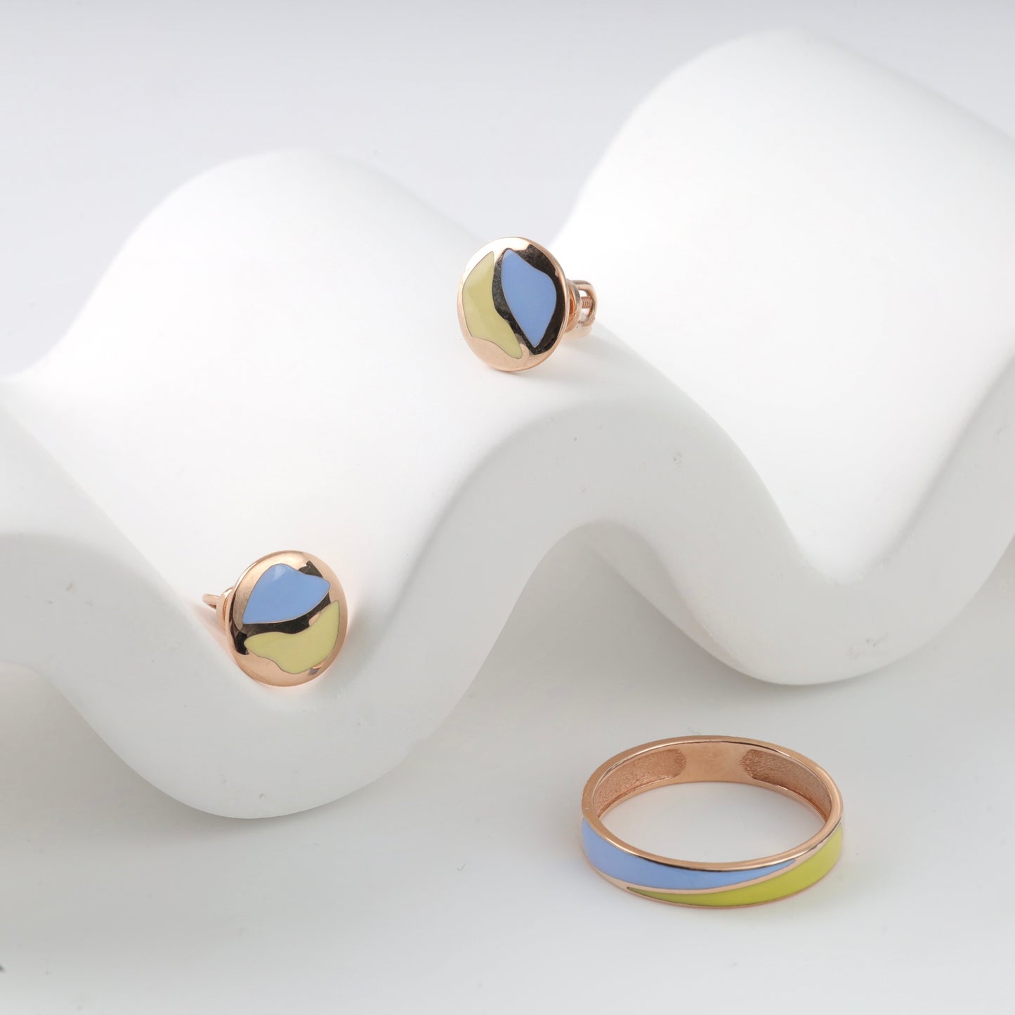 Sophisticated 14K (585) Rose Gold patriotic jewelry set featuring a minimalist wavy enamel ring and matching round stud earrings with vibrant blue and yellow accents, elegantly displayed on a white wavy decorative prop.