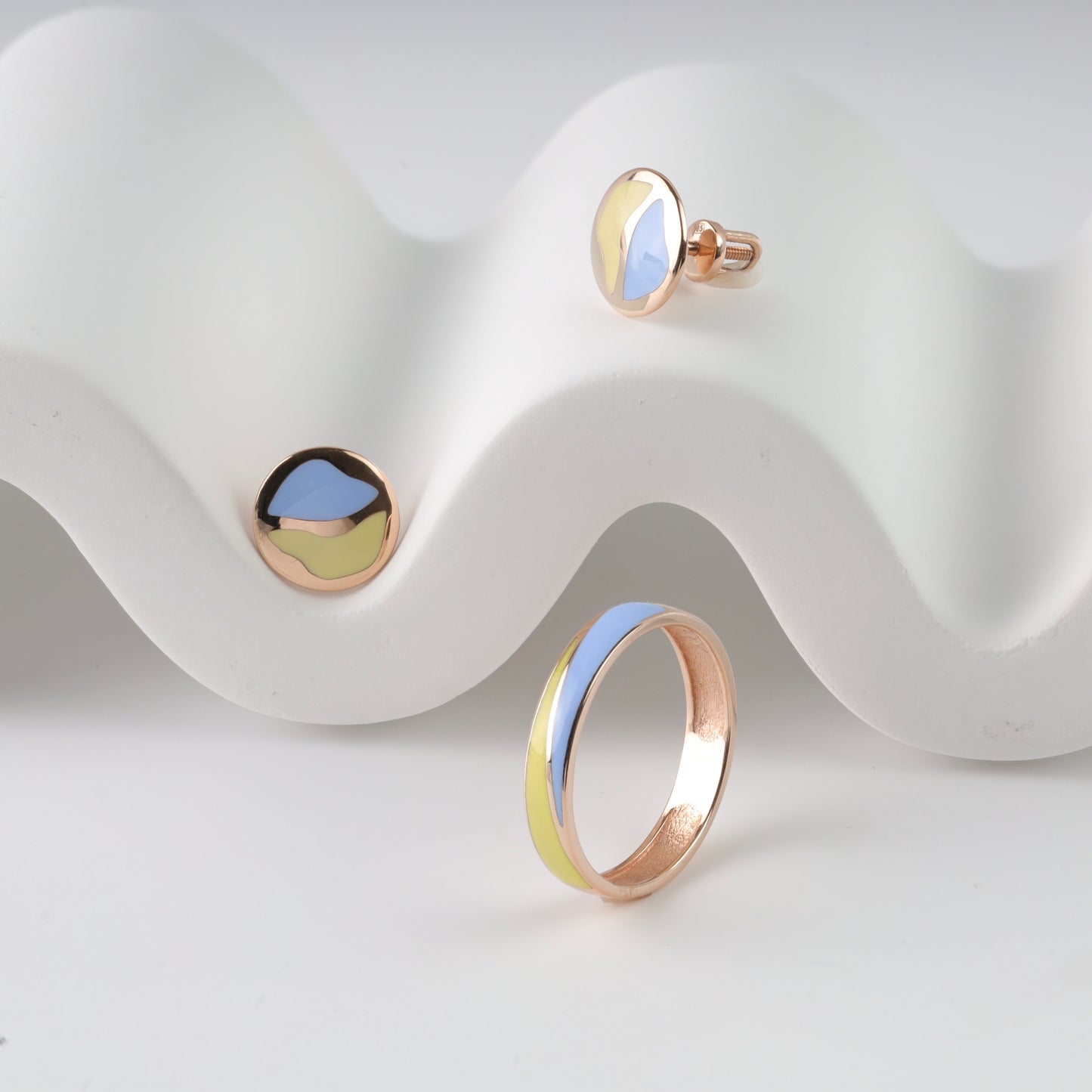 Sophisticated 14K (585) Rose Gold patriotic jewelry set featuring a minimalist wavy enamel ring and matching round stud earrings with vibrant blue and yellow accents, elegantly displayed on a white wavy decorative prop.