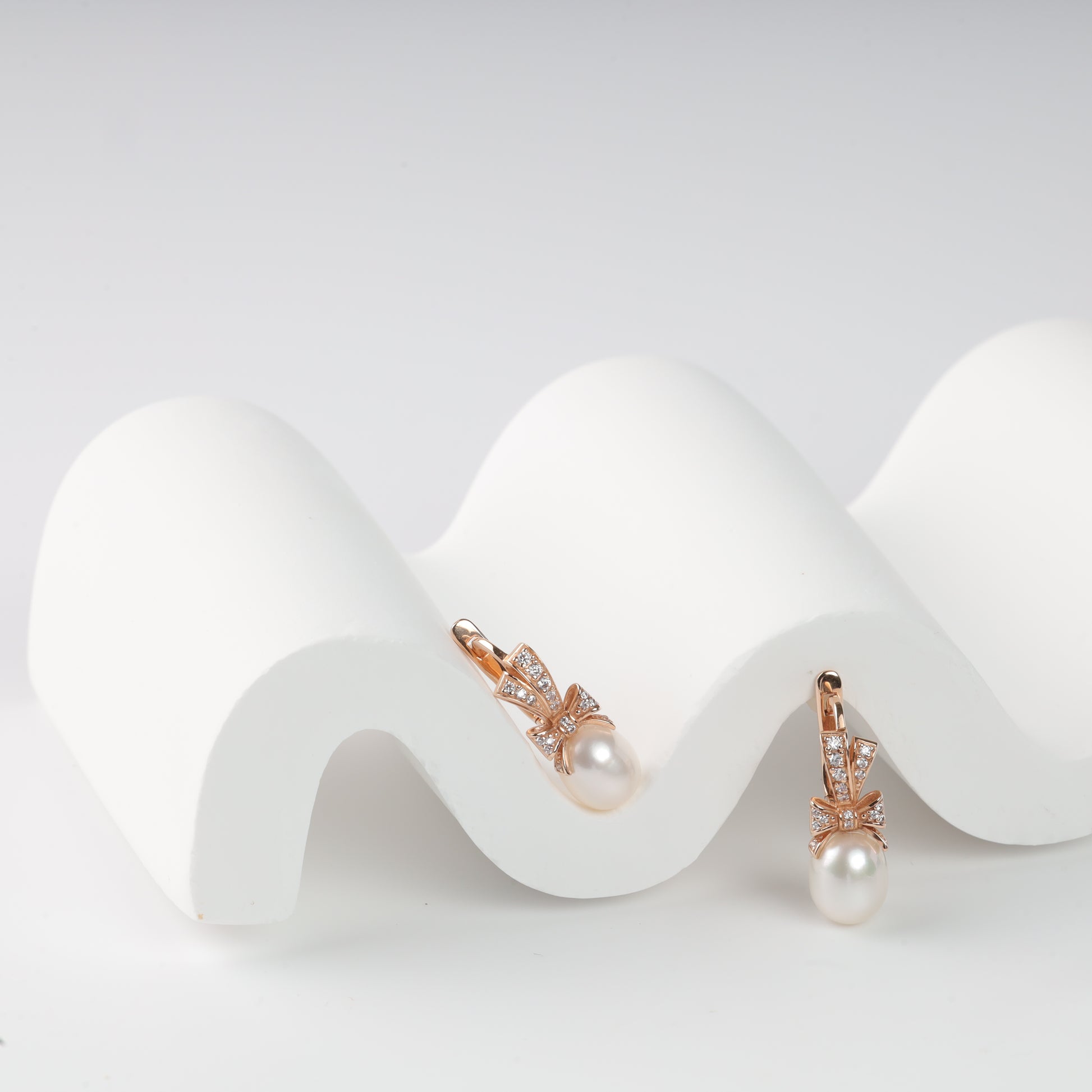 Elegant 14K (585) Rose Gold drop earrings featuring a sparkling zirconia-set bow and a lustrous teardrop pearl, secured with a classic English lock.