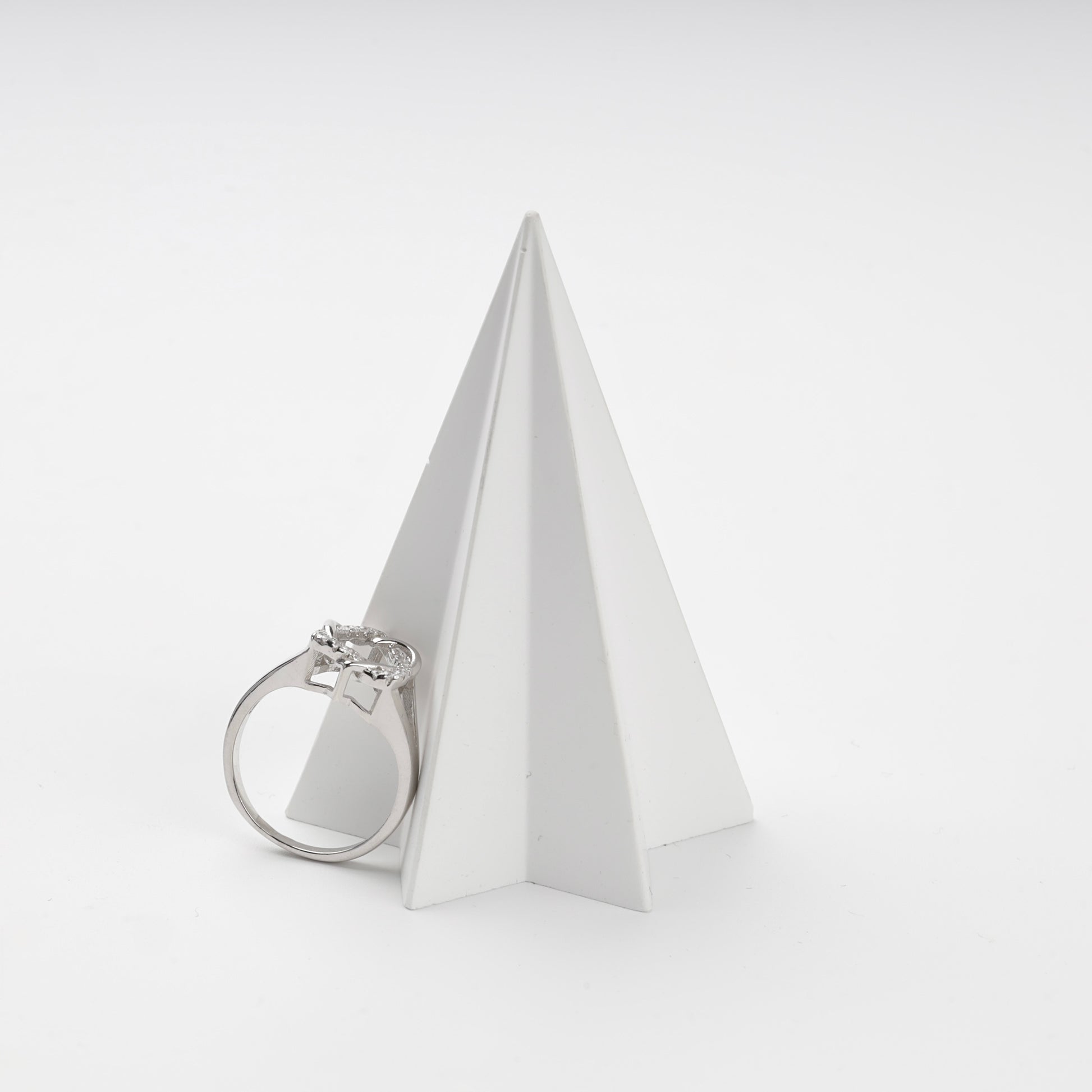 Silver cubic zirconia ring displayed beside a white geometric stand