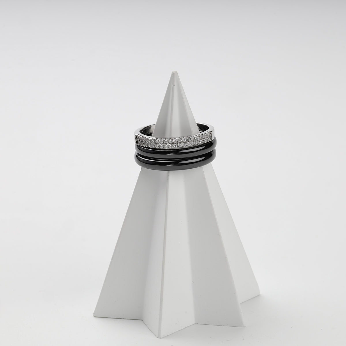 Three-ring black ceramic set displayed on a white geometric stand