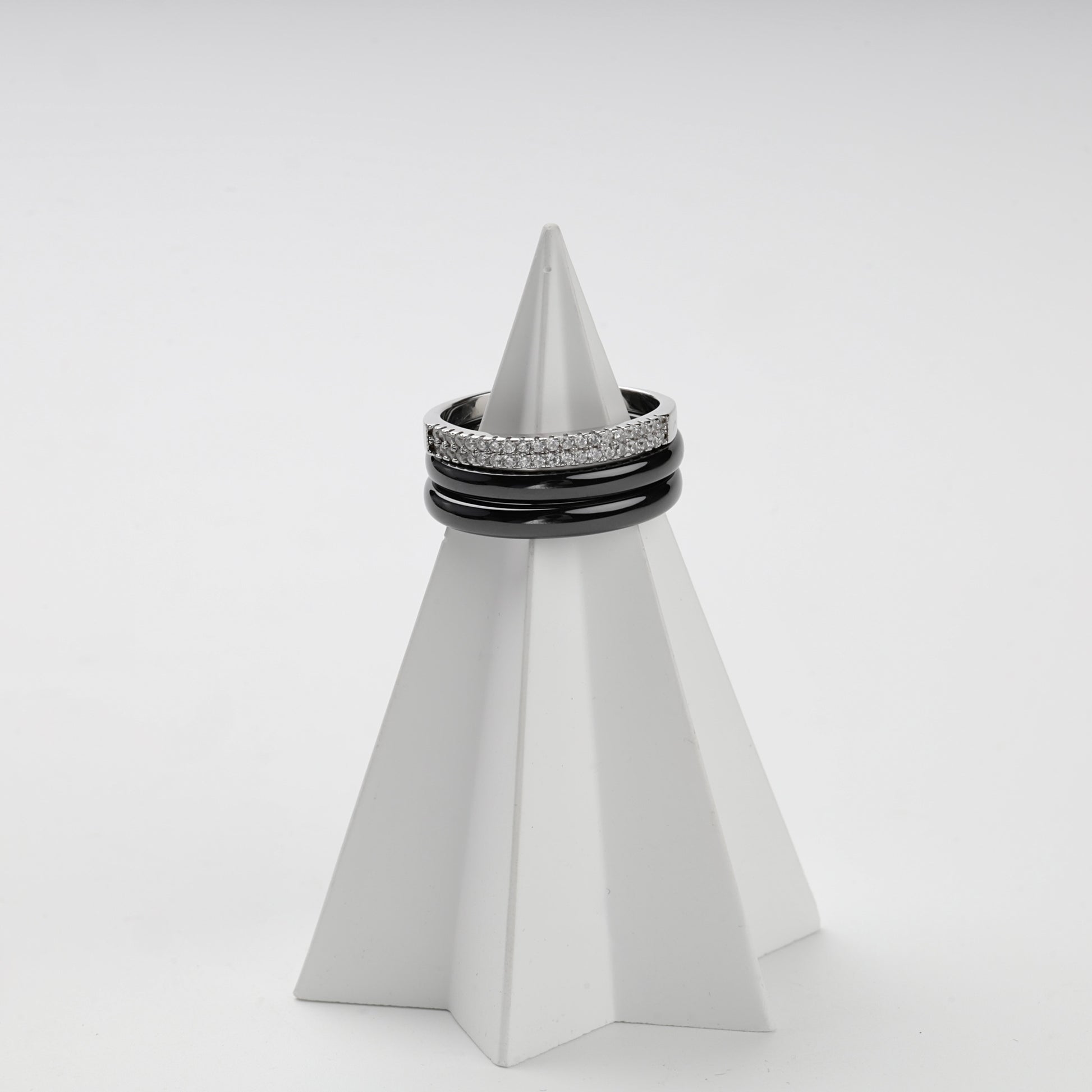 Three-ring black ceramic set displayed on a white geometric stand