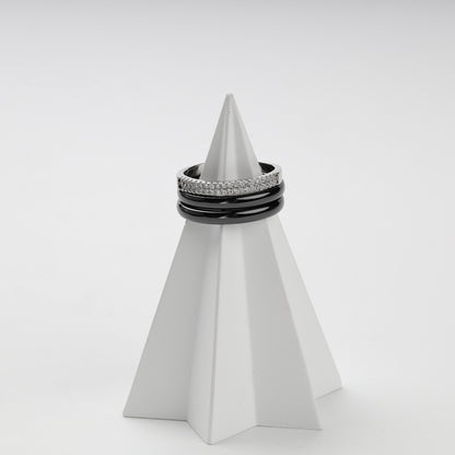 Three-ring black ceramic set displayed on a white geometric stand