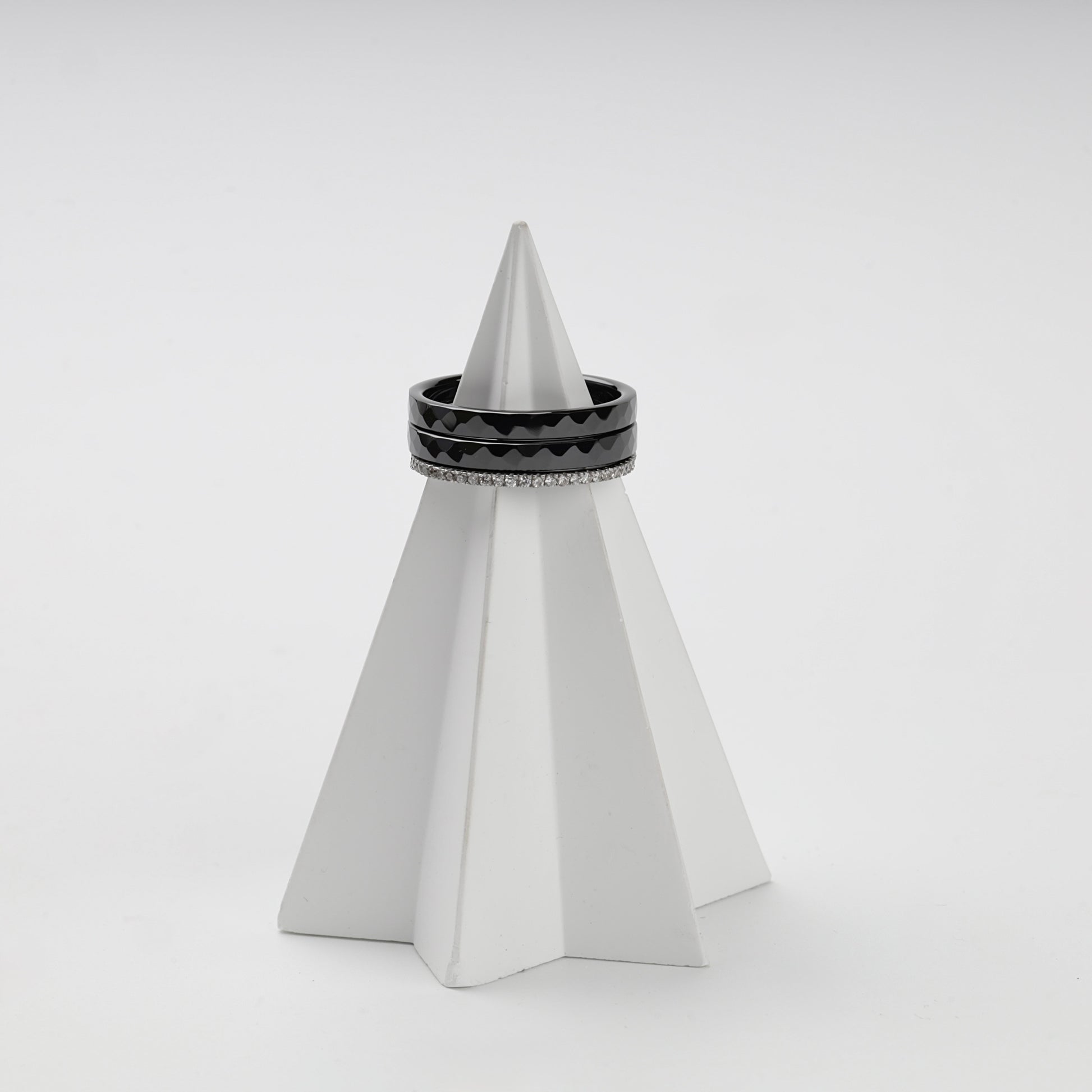 Three-ring black ceramic and clear cubic zirconia set on a white stand